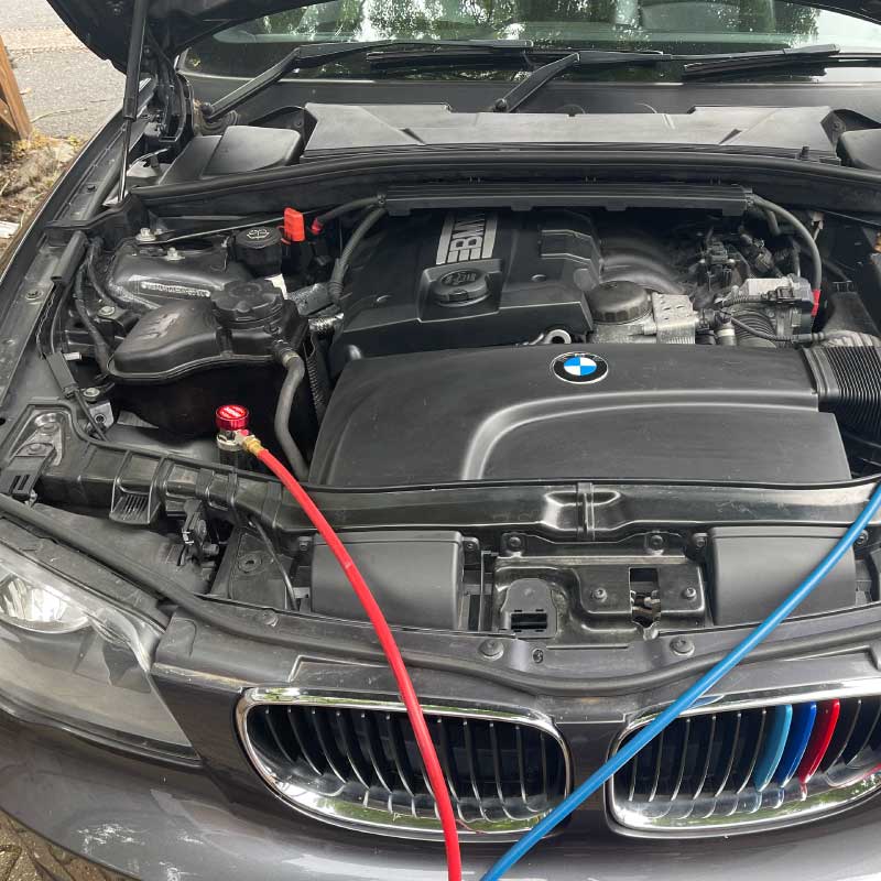 Air con regas hoses connected to a car engine bay during a service